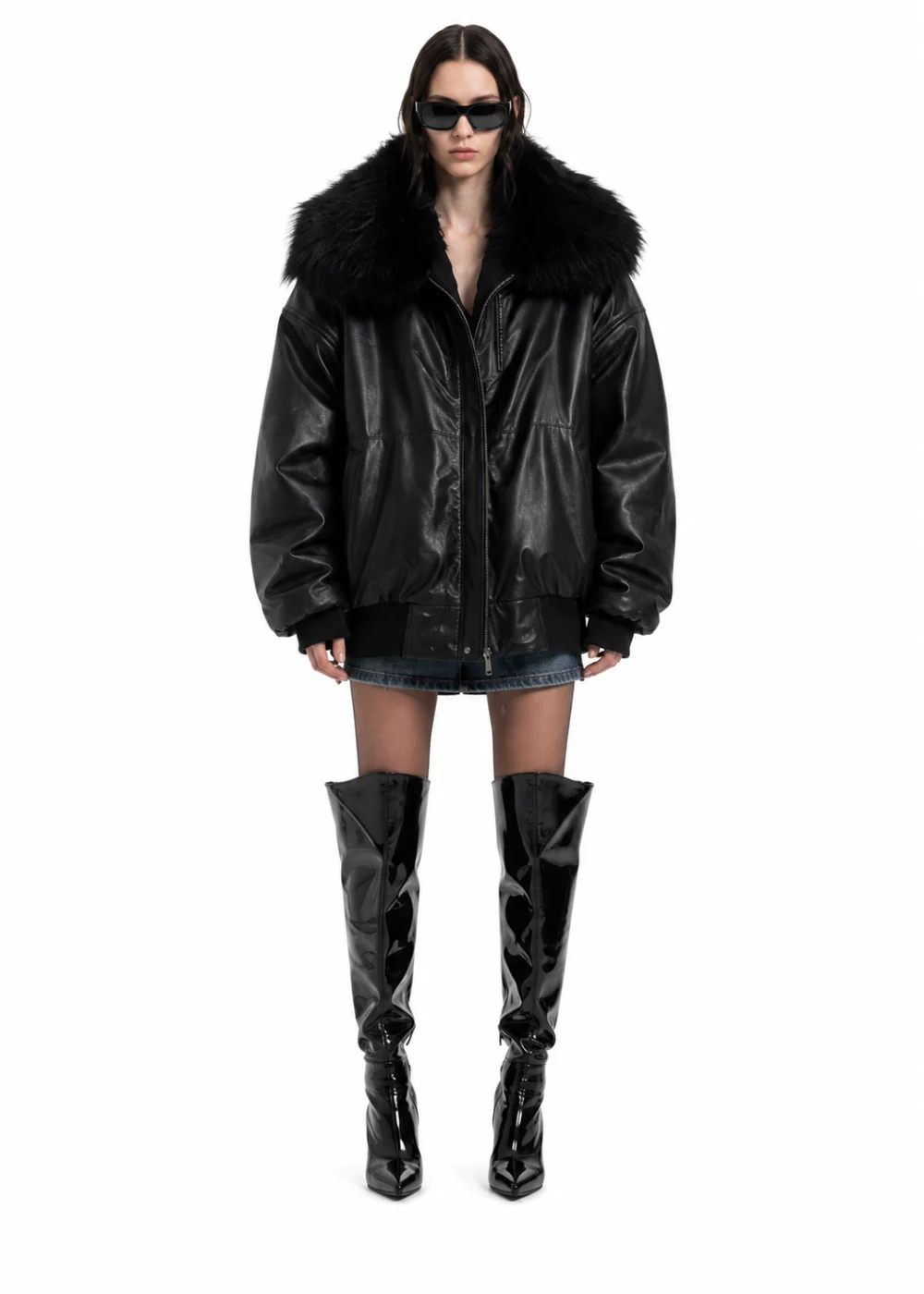 Woman in a black leather bomber with a large fur collar, denim shorts, sunglasses and glossy over-the-knee boots on white.