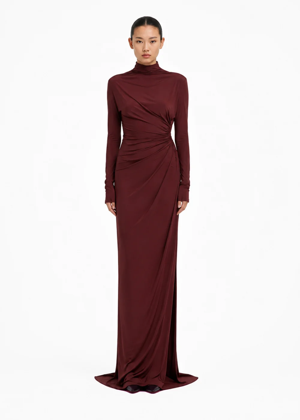Woman in a floor-length burgundy high-neck dress with long sleeves and gathered draping at the waist, full length on white.