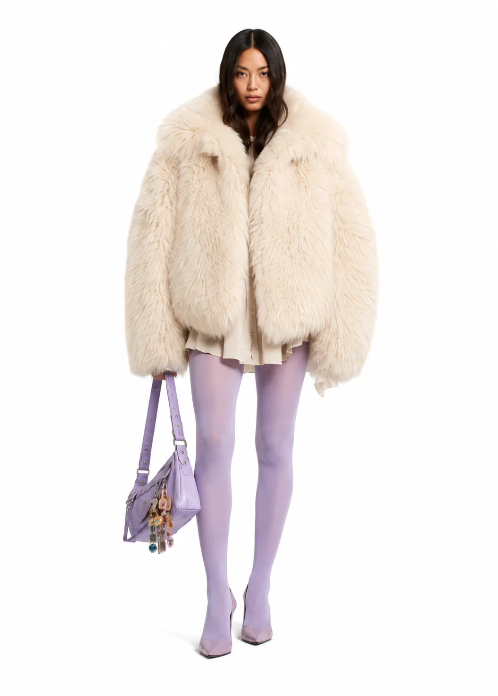 Woman in a cream faux fur jacket, lavender tights and a lilac bag, standing front-on on a white background.