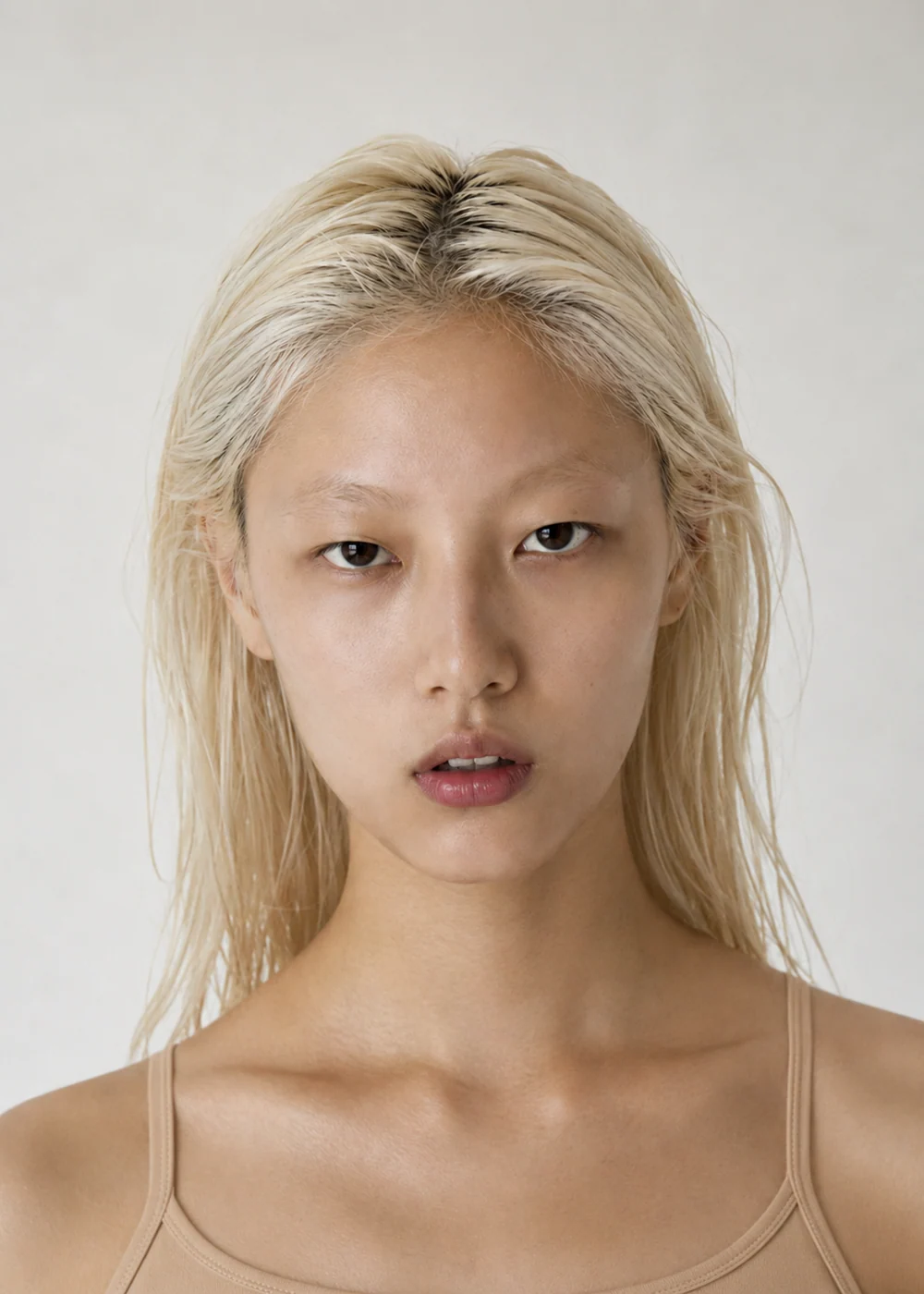 Portrait of a young woman with bleached blonde hair and dark eyebrows, beige camisole, soft front light.