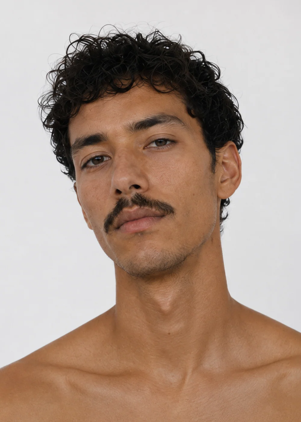 Portrait of a man with dark curly hair and a thin moustache, bare shoulders, against a light background.